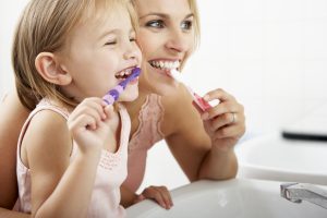 A mother and her young daughter brushing their teeth.